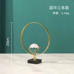 Modern gold decorative ornament with a circular design and crystal sphere on a black base.