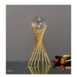 Modern gold decorative sculpture with glass orb on reflective surface.