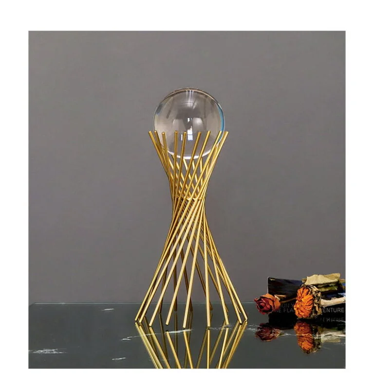 Modern gold decorative sculpture with glass orb on reflective surface.