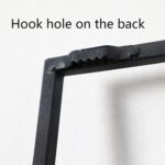 Close-up of a hook hole on the back of a black aluminium frame for wall art.