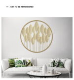 Gold leaf metal wall art above a modern white sofa with green leaf cushions.