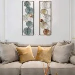 Modern metal wall art with leaf designs above a beige sofa with gold cushions.