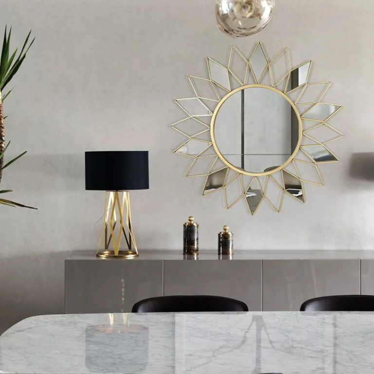 Modern luxury home decor with gold sunburst wall mirror and elegant table lamp.