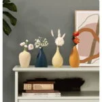 Modern decorative vases with flowers on a shelf, featuring abstract wall art in the background.