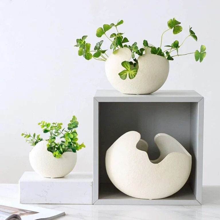 Modern decorative vases with green plants on a white shelf.