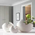 Modern white ceramic vases with green flowers on a table in a stylish home interior.