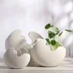Modern ceramic vases with unique shapes and a plant, perfect for luxury home decor.