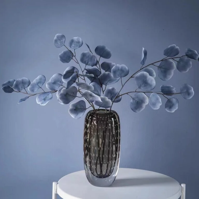Modern glass vase with blue foliage on a white table, luxury home decor.