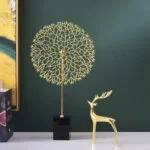 Gold decorative tree sculpture and deer figurine on a table against a green wall.