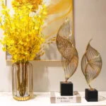 Modern home decor with yellow flowers in a vase and gold sculptures on a table.
