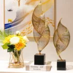 Modern gold sculptures and floral arrangement on a table with abstract wall art.