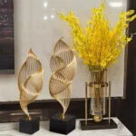 Elegant gold sculptures and yellow floral arrangement on a marble surface, modern home decor.