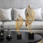 Modern gold decorative sculptures on a black base in a luxury living room setting.