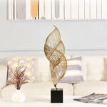 Modern gold sculpture on a black base in a stylish living room setting.