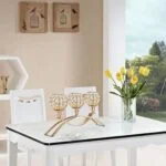 Elegant gold candle holder on a modern dining table with yellow tulips and wall art in the background.