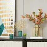 Modern home decor with gold vase, decorative branches, and framed wall art.