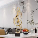 Modern gold sculpture on a marble base in a luxury living room setting.