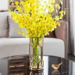 Elegant yellow flowers in a gold vase on a modern black marble table.