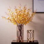 Elegant yellow floral arrangement in a decorative glass vase on a wooden table.