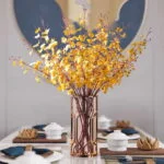 Elegant dining table with a decorative vase of yellow flowers and modern tableware.