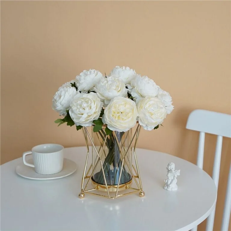Elegant white flowers in a gold geometric vase on a table with a cup and small figurine.