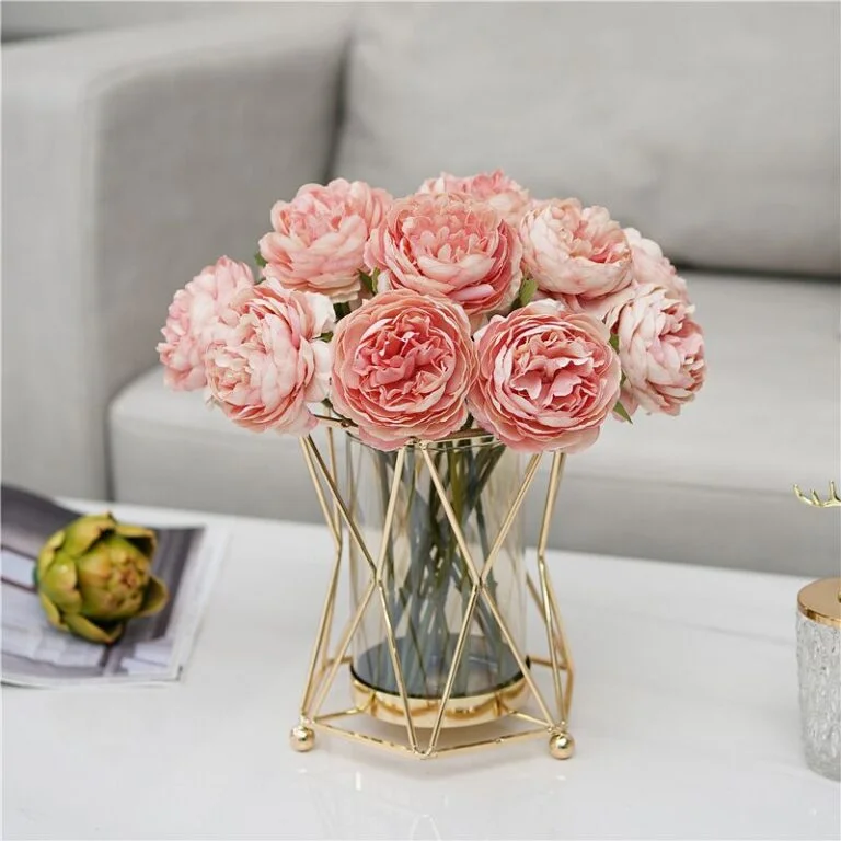 Elegant pink flowers in a gold geometric vase on a modern coffee table.