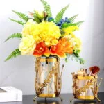 Elegant gold decorative vases with vibrant flowers on a marble surface.