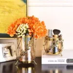 Elegant gold and glass vases with orange flowers on a modern decor table.