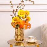 Elegant gold vase with vibrant yellow and orange flowers on a modern table.