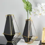 Modern black and gold geometric vases with flowers on a table.