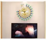 Peacock-themed decorative wall clock above a television, modern home decor.