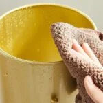Close-up of a hand cleaning a gold decorative vase with a cloth.
