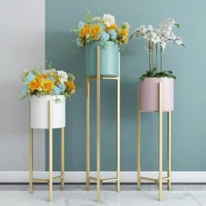 Modern decorative planters with flowers on gold stands against a blue wall.