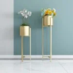 Gold metal planters with flowers against a blue wall, modern home decor.