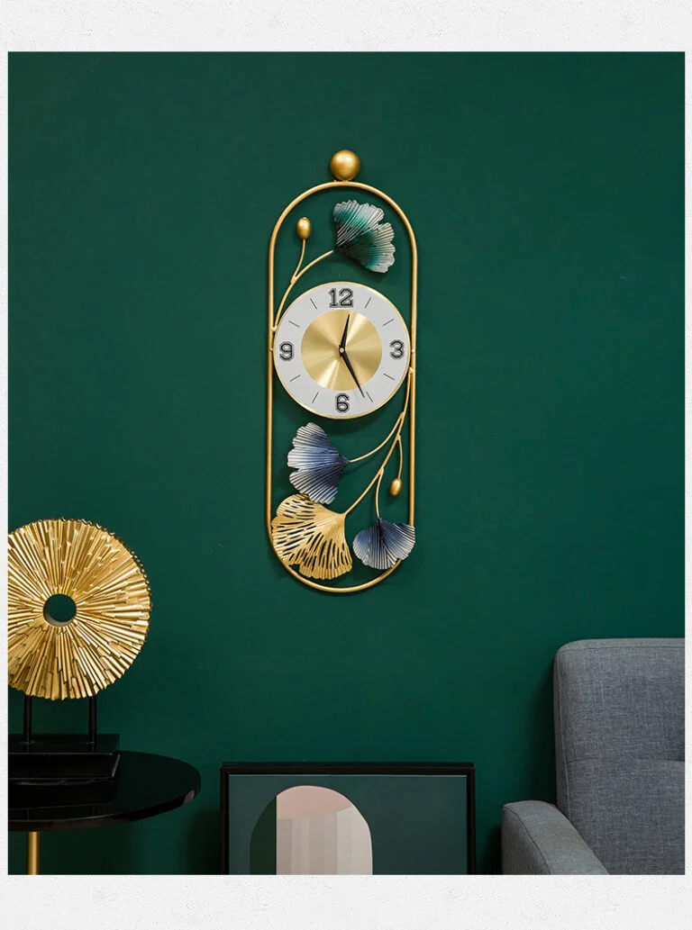 Modern decorative wall clock with gold and green leaf design on a dark green wall.