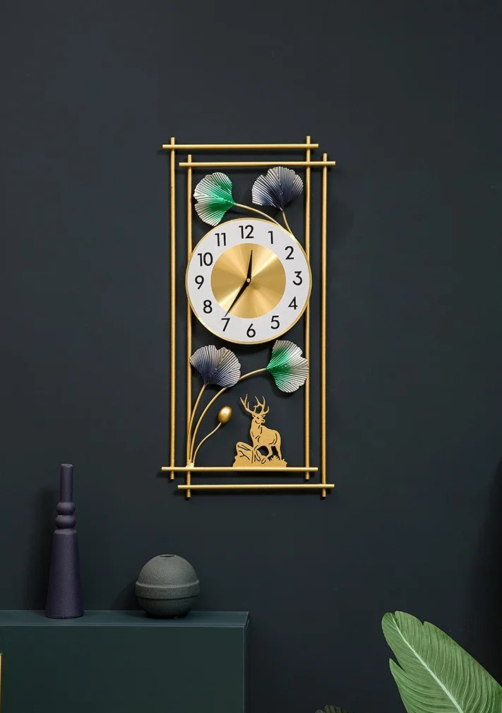 Modern decorative wall clock with gold frame and floral accents on dark wall.