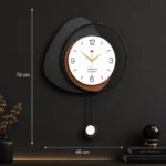 Modern decorative wall clock with geometric design and pendulum on a dark wall.