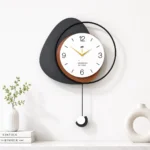 Modern decorative wall clock with geometric design and pendulum, styled with vases and books on a shelf.