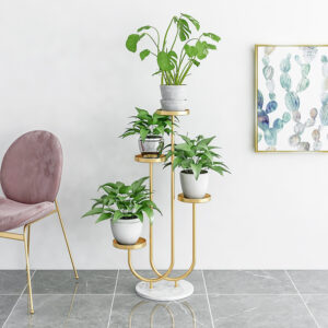Modern gold plant stand with green plants and framed cactus wall art in a stylish room.