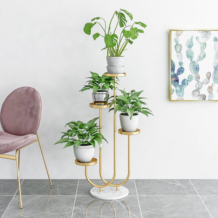 Modern gold plant stand with green plants and framed cactus wall art in a stylish room.