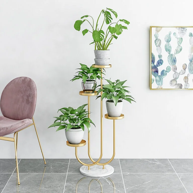 Modern gold plant stand with green plants and framed cactus wall art in a stylish room.